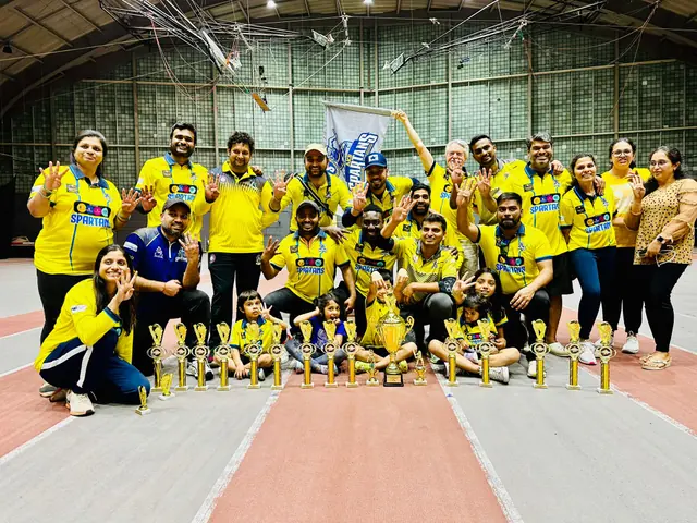 Cricketers in yellow shirts posing with trophies inside a sports facility.