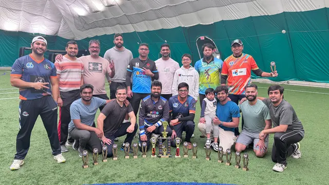 A group of cricketers gathered with trophies on an indoor field.