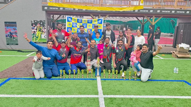 A cricket team posing with trophies on an indoor playing surface.